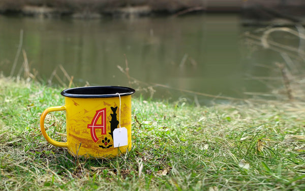 Angler's Coffee sachet brewing in the yellow Angler's camp mug by the river, tag over the rim